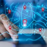 Mão de gestor interagindo com interface digital de mapa e pins de localização em tempo real, ilustrando o uso de sistemas inteligentes para o rastreamento de veículos e monitoramento de frota.