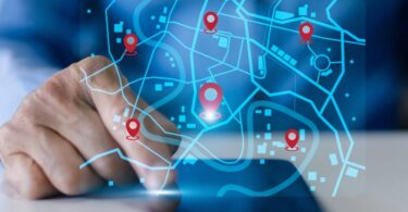 Mão de gestor interagindo com interface digital de mapa e pins de localização em tempo real, ilustrando o uso de sistemas inteligentes para o rastreamento de veículos e monitoramento de frota.