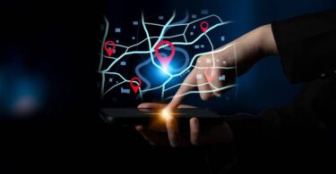 Mão de usuário operando smartphone com interface de mapa digital e pins de geolocalização flutuantes, demonstrando o uso do otimizador de rotas do Google para planejamento logístico avançado.