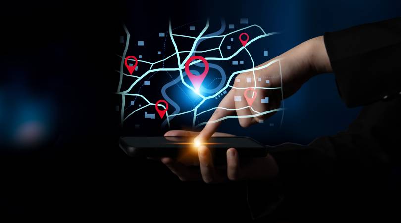Mão de usuário operando smartphone com interface de mapa digital e pins de geolocalização flutuantes, demonstrando o uso do otimizador de rotas do Google para planejamento logístico avançado.