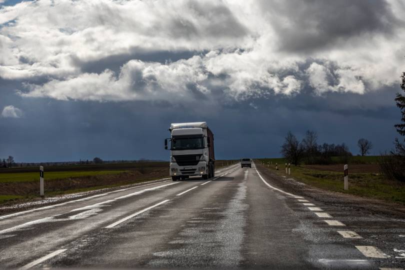 Um caminhão dirigindo por uma estrada sob um céu nublado. Representa os dados de condições climáticas oferecidos pela API Weather.