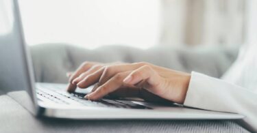 Mão em close-up utilizando um computador portátil. Uso da tecnologia de conexão online para negócios, educação e comunicação.