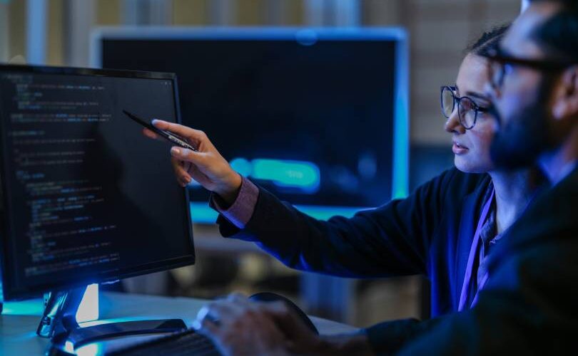 Desenvolvedores analisando linhas de código em um monitor de alta resolução, representando a infraestrutura robusta e a engenharia por trás do Google Antigravity.