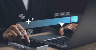 Mão tocando tela de celular com elementos gráficos de barra de pesquisa e faíscas de IA, representando as funcionalidades do Microsoft Copilot e Google Gemini em ambiente corporativo.