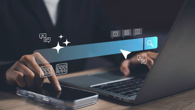 Mão tocando tela de celular com elementos gráficos de barra de pesquisa e faíscas de IA, representando as funcionalidades do Microsoft Copilot e Google Gemini em ambiente corporativo.