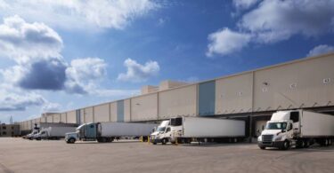 Fileira de caminhões de carga estacionados em docas de um grande centro de distribuição, ilustrando a logística Just in Case para garantir a disponibilidade de produtos e evitar rupturas no estoque.