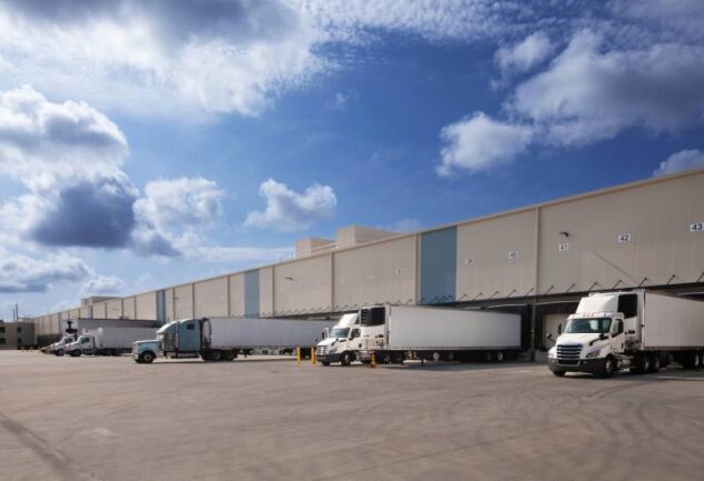 Fileira de caminhões de carga estacionados em docas de um grande centro de distribuição, ilustrando a logística Just in Case para garantir a disponibilidade de produtos e evitar rupturas no estoque.