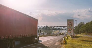 Caminhão de carga trafegando em rodovia com sinalização de fiscalização, representando a eficiência logística em operações regionais de transporte e distribuição de mercadorias.