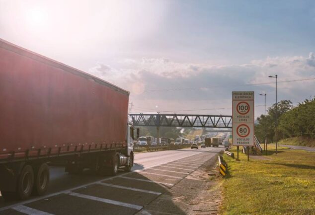 Caminhão de carga trafegando em rodovia com sinalização de fiscalização, representando a eficiência logística em operações regionais de transporte e distribuição de mercadorias.