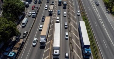 Vista aérea de rodovia com fluxo intenso de caminhões e carros, ilustrando a aplicação de tecnologias de roteirização para reduzir opex em frotas logísticas.