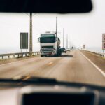 Caminhão de transporte pesado trafegando em estrada retilínea sob luz solar, representando o fluxo contínuo e o planejamento de roteirização para middle mile para otimizar o tempo de trânsito.