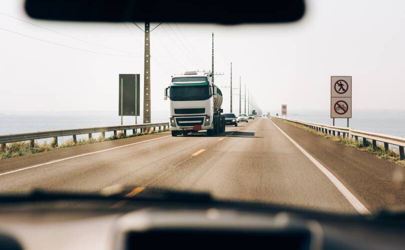 Caminhão de transporte pesado trafegando em estrada retilínea sob luz solar, representando o fluxo contínuo e o planejamento de roteirização para middle mile para otimizar o tempo de trânsito.