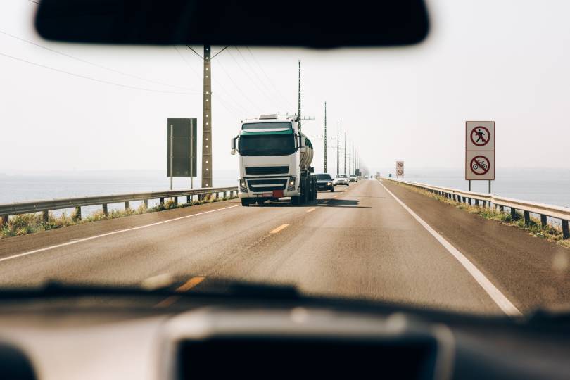 Caminhão de transporte pesado trafegando em estrada retilínea sob luz solar, representando o fluxo contínuo e o planejamento de roteirização para middle mile para otimizar o tempo de trânsito.