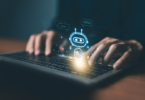 Close de usuário interagindo com computador onde surge um ícone de robô com a inscrição "AI", representando a integração de sistemas de IA corporativa para suporte e eficiência operacional.