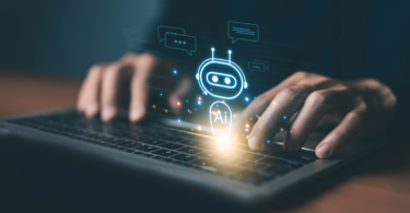 Close de usuário interagindo com computador onde surge um ícone de robô com a inscrição "AI", representando a integração de sistemas de IA corporativa para suporte e eficiência operacional.
