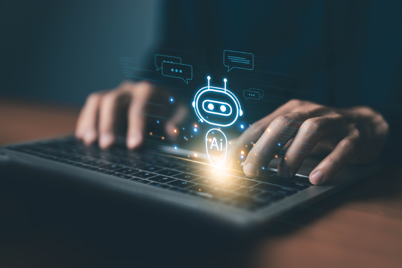 Close de usuário interagindo com computador onde surge um ícone de robô com a inscrição "AI", representando a integração de sistemas de IA corporativa para suporte e eficiência operacional.