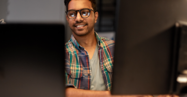 Desenvolvedor sorrindo em frente a múltiplos monitores no escritório, demonstrando a facilidade e agilidade trazidas pelo Google Antigravity na automação corporativa com inteligência artificial.