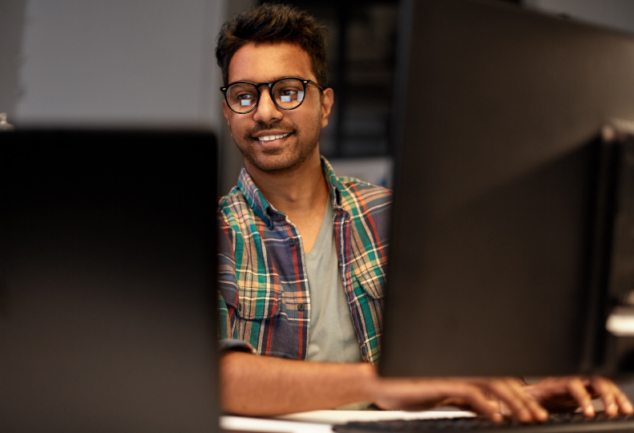 Desenvolvedor sorrindo em frente a múltiplos monitores no escritório, demonstrando a facilidade e agilidade trazidas pelo Google Antigravity na automação corporativa com inteligência artificial.