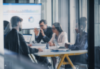 Equipe de líderes comerciais e de dados reunida em sala corporativa moderna, analisando gráficos em uma grande tela e em notebooks para avaliar soluções de prospecção.