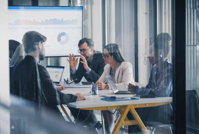 Equipe de líderes comerciais e de dados reunida em sala corporativa moderna, analisando gráficos em uma grande tela e em notebooks para avaliar soluções de prospecção.
