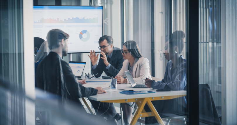 Equipe de líderes comerciais e de dados reunida em sala corporativa moderna, analisando gráficos em uma grande tela e em notebooks para avaliar soluções de prospecção.