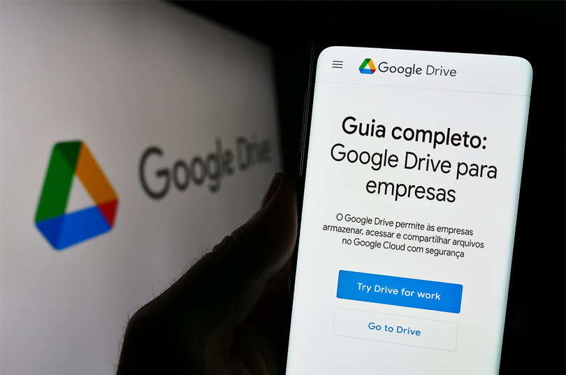 Close de uma pessoa segurando um celular. Na tela do celular, está a interface do Google Drive com o texto "Guia Completo: Google Drive para empresas".