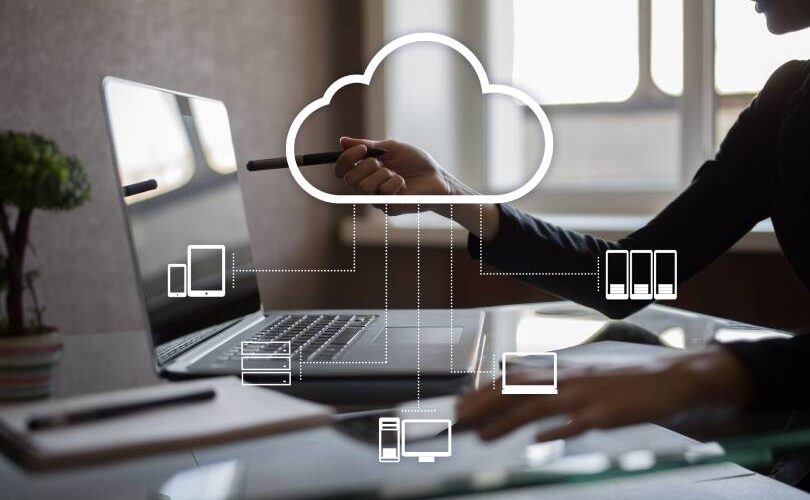 Uma mulher sentada em uma mesa com um laptop e uma nuvem acima dela. Ícones em destaque que representam tecnologia de computação em nuvem.